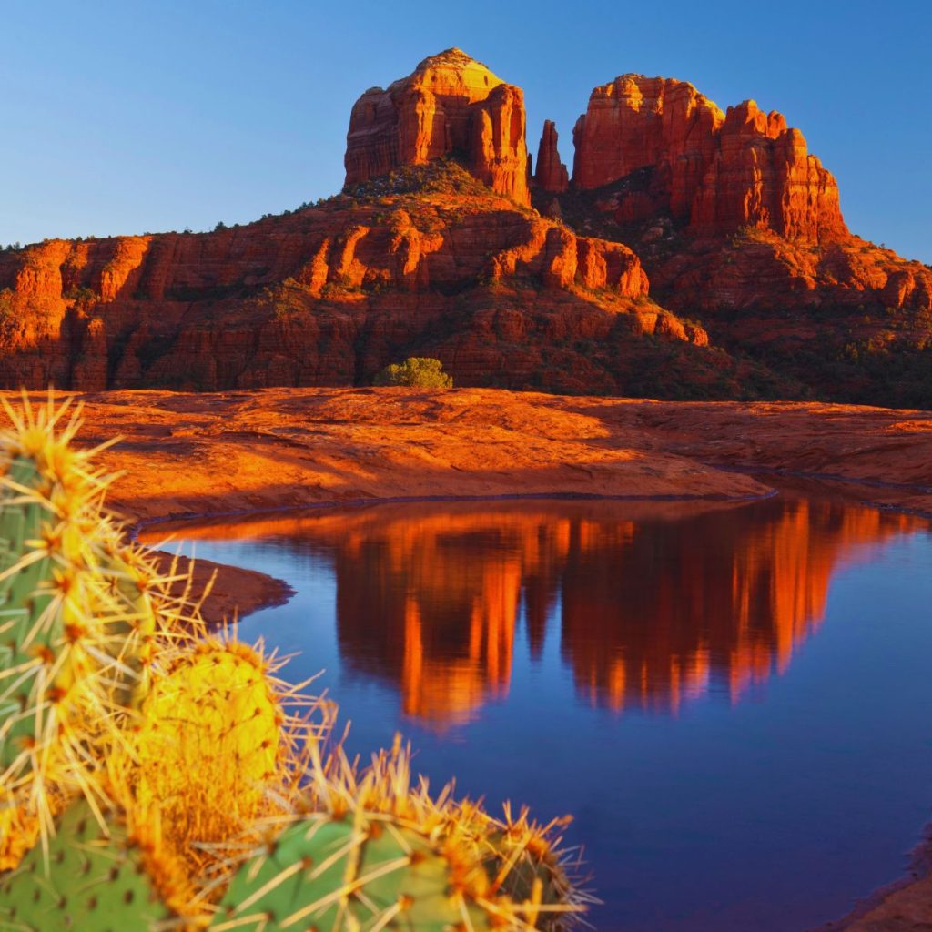 sedona mountains and rock formations with orange dirt and a lake in front of them